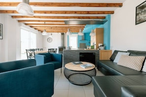 A modern living room with a fireplace, blue sofas, a round coffee table, and wooden beams on the ceiling.