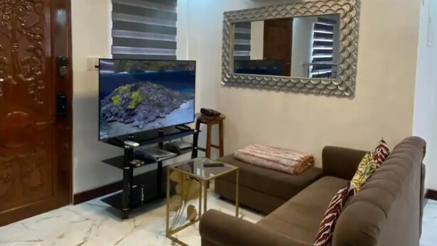 Un saló amb terra de marbre, un sofà marró, una televisió i un mirall decoratiu.
