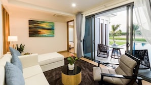 A modern living room with a white sofa, a round coffee table, and a painting on the wall. There is a glass door leading to a balcony with outdoor furniture. - SAKI VILI HO TRAM (Ho Chi Minh City)