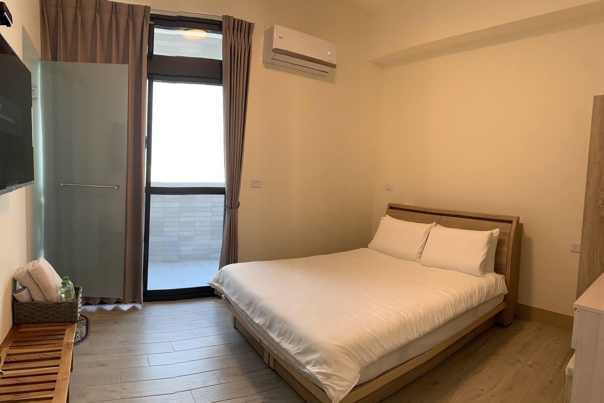 A hotel room with a bed, a wooden bench, a wardrobe, and an air conditioning unit.