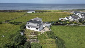 A coastal residential area with houses, a grassy field, and a view of the sea. - Angorfa -  a coastal property that sleeps 8 guests  in 4 bedrooms (Caernarfon)