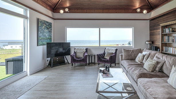 A spacious living room with a large window overlooking the sea, a fireplace, and a bookshelf. - Angorfa -  a coastal property that sleeps 8 guests  in 4 bedrooms (Caernarfon)