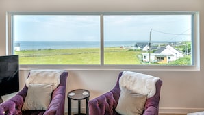 A room with two purple armchairs, a small round table, and a large window offering a view of the sea and houses. - Angorfa -  a coastal property that sleeps 8 guests  in 4 bedrooms (Caernarfon)