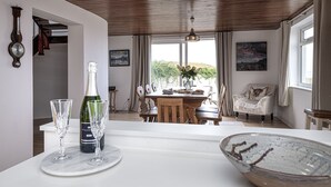 A dining area with a wooden table, chairs, and a view of greenery outside. - Angorfa -  a coastal property that sleeps 8 guests  in 4 bedrooms (Caernarfon)