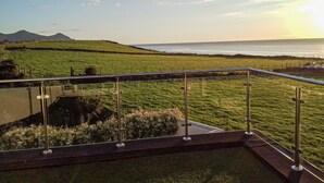 A view from a balcony overlooking a grassy field with a body of water and distant hills. - Angorfa -  a coastal property that sleeps 8 guests  in 4 bedrooms (Caernarfon)