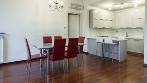A modern kitchen with white cabinets, a central island with bar stools, and a dining area with red chairs and a glass table. - Scipione by Mmega (Florence)