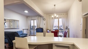 A modern kitchen with a white countertop, a dining area with a table and chairs, a blue sofa, and a view of the city through large windows. - Scipione by Mmega (Florence)