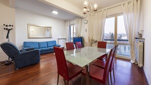 A modern living room with a glass dining table, red chairs, a blue sofa, and a view of the city through large windows. - Scipione by Mmega (Florence)