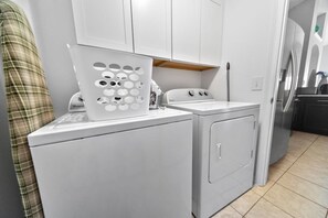 A compact laundry area with a washing machine, dryer, and a drying rack. - Private 4 BDR Oasis in Kissimmee with Pool | BBQ (Kissimmee)