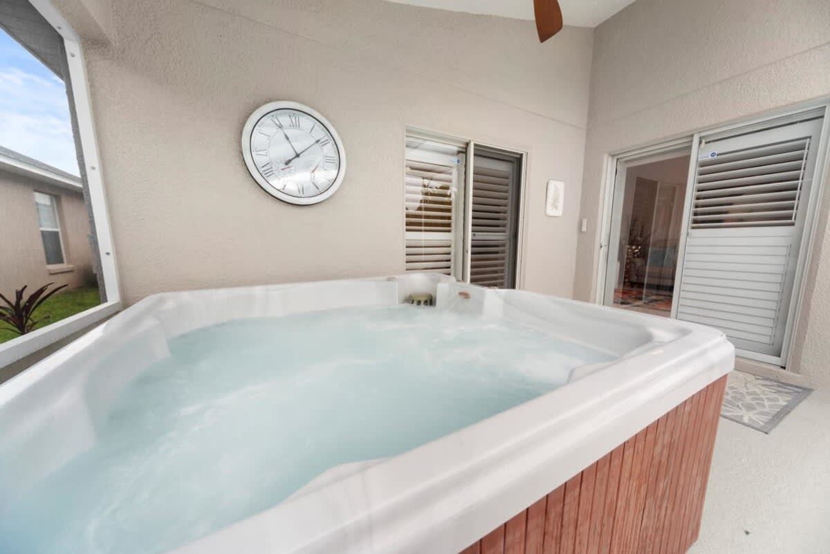 A hot tub with a clock on the wall, a window, and a door with blinds.