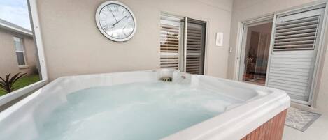 A hot tub with a clock on the wall, a window, and a door with blinds.