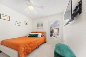 Quarto com cama, ventoinha no teto, janela com persianas e televisão na parede.