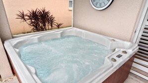 A hot tub with a clock on the wall, surrounded by a beige wall and some plants. - Private 4 BDR Oasis in Kissimmee with Pool | BBQ (Kissimmee)