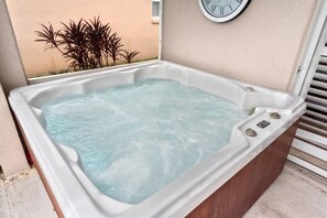 A hot tub with a clock on the wall, surrounded by a beige wall and some plants. - Private 4 BDR Oasis in Kissimmee with Pool | BBQ (Kissimmee)