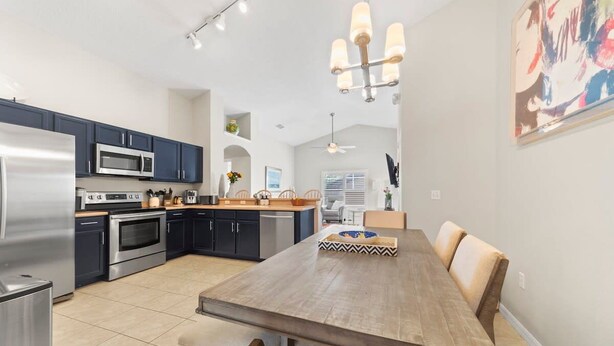 A modern kitchen with stainless steel appliances, a dining area with a wooden table, and a ceiling fan. - Private 4 BDR Oasis in Kissimmee with Pool | BBQ (Kissimmee)