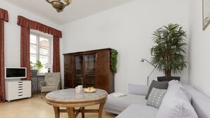 A living room with a round wooden table, a grey sofa, a cabinet, and a large plant. - Atmospheric Apartment in the Old Town | Desk for Work (Warszawa)