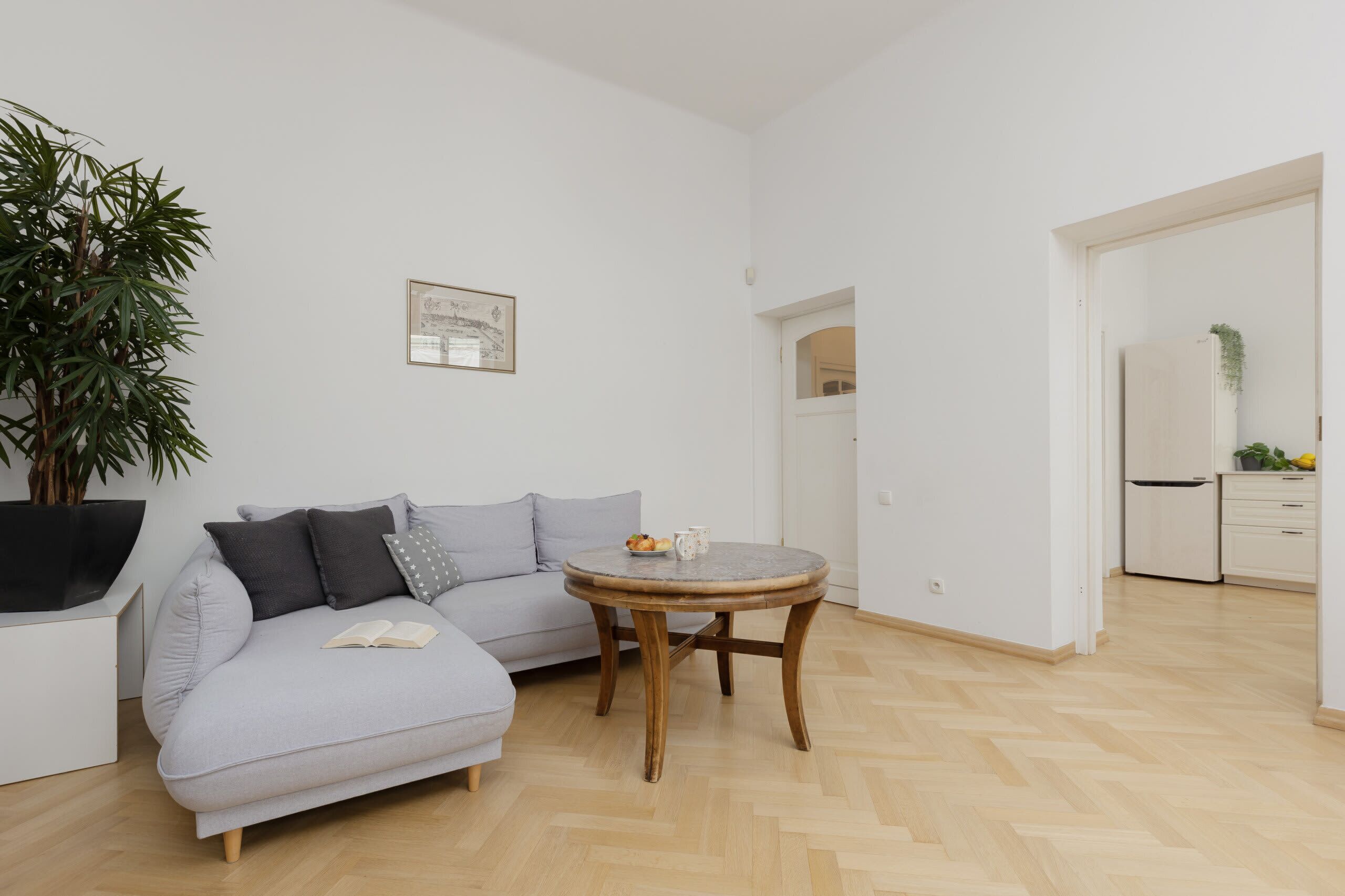 A modern living room with a grey sofa, a round wooden coffee table, and a large potted plant.