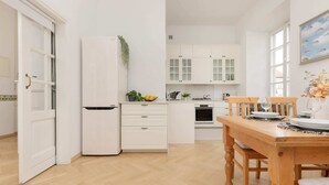 A modern kitchen with white cabinetry, a wooden dining table, and a view of the adjacent living area. - Atmospheric Apartment in the Old Town | Desk for Work (Warszawa)