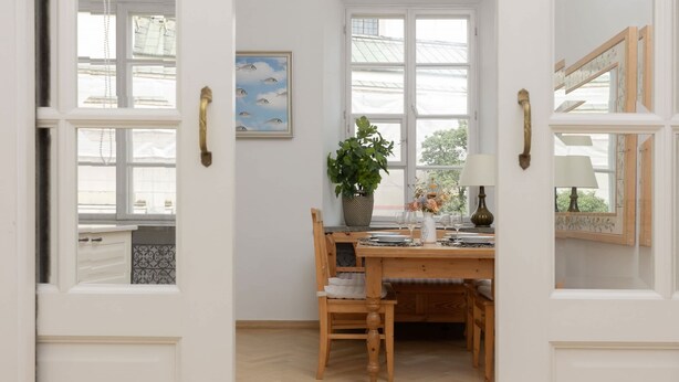 A room with a wooden dining table, chairs, a potted plant, and a window with a view of the outside. - Atmospheric Apartment in the Old Town | Desk for Work (Warszawa)