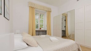 A neatly arranged bedroom with a bed, a window with curtains, a mirror, and a wardrobe. - Atmospheric Apartment in the Old Town | Desk for Work (Warszawa)