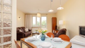 Un comedor con una mesa dispuesta para cuatro personas, un florero con flores y un televisor sobre un mueble.