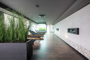 Un espace spa moderne comprenant une rangée de chaises longues, un téléviseur fixé au mur et une plante en pot.