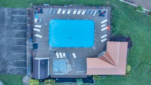 Vista aérea de una piscina con solárium, sillas de descanso y una zona cubierta.