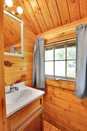 A wooden cabin bathroom with a white sink, wooden cabinets, a mirror, and a window with curtains.