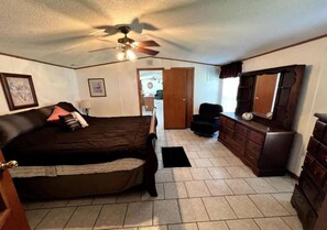 A bedroom with a bed, a dresser, a chair, a ceiling fan, and a door leading to another room. - Spacious Model Home in Bloomington (Bloomington)
