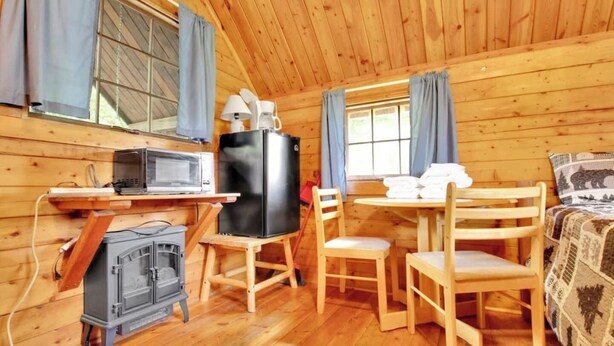 Ein gemütliches Blockhaus mit Holzwänden, einem Esstisch mit Stühlen, einer Mikrowelle, einem Kühlschrank und einem Kamin.