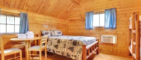 Una habitación acogedora tipo cabaña de madera, con una cama, una mesa y sillas, y un ventanal con cortinas.