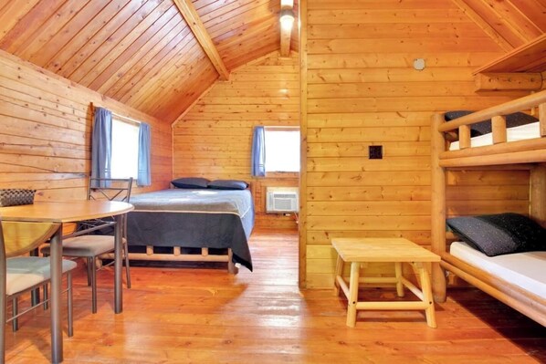 A cozy cabin with a wooden interior, a bunk bed, a dining area, and a small table.