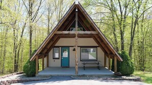 A small, single-story cabin with a pitched roof, a front door, and a bench outside. - Stunning Aframe Cabin with Deck (Bloomington)