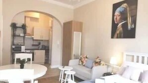 A modern living room with a white sofa, a dining table, and a kitchen in the background. - Lovely Renovated Large Spacious Georgian Studio (Dublin 1)