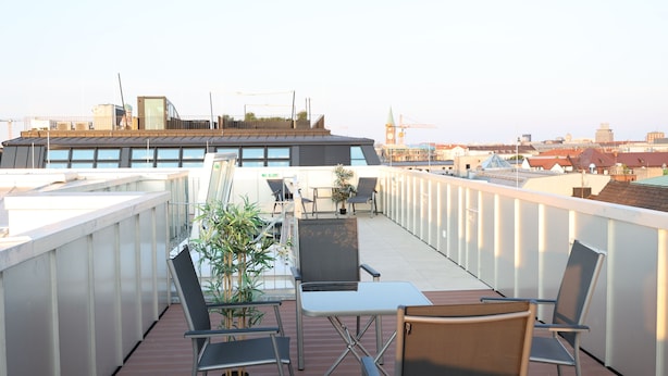 En takterrass med utomhusmöbler, en krukväxt och utsikt över stadsbilden.