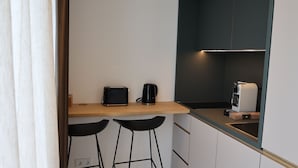 Ett litet, praktiskt kök med en brödrost, en kaffebryggare och en vattenkokare på en bänkskiva i trä. Det finns två svarta barstolar och ett litet diskhoområde.