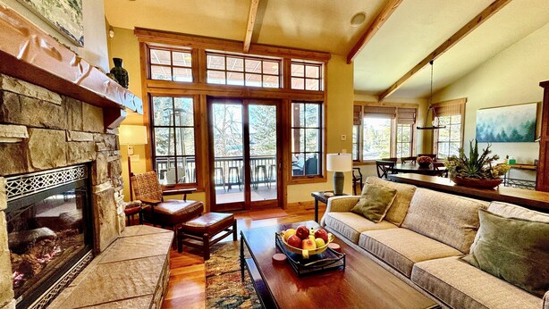 A spacious living room with a stone fireplace, large windows, a wooden ceiling, and a cozy seating area with a coffee table.