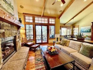 A spacious living room with a stone fireplace, large windows, a wooden ceiling, and a cozy seating area with a coffee table.
