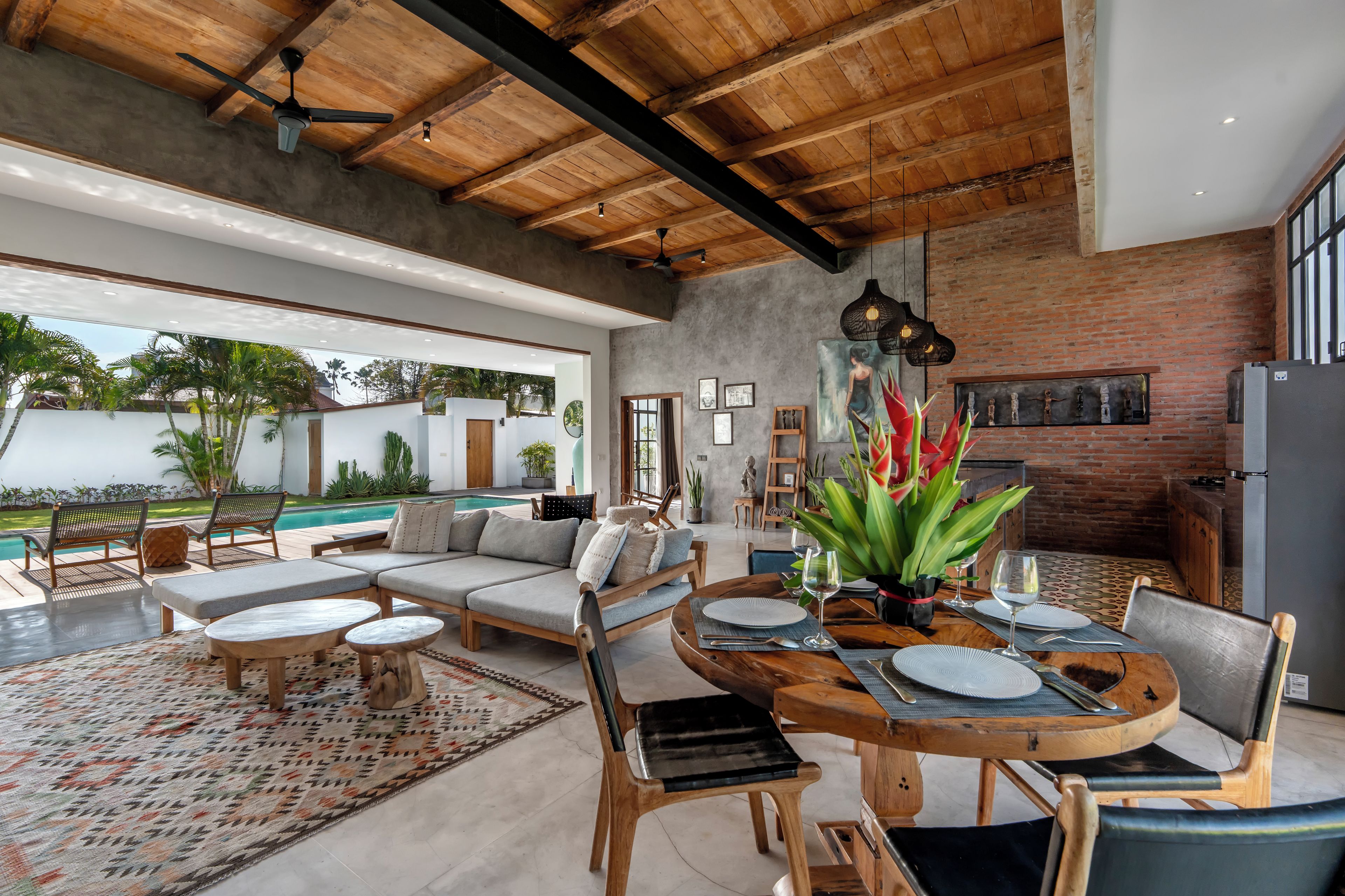 A modern interior with a dining area, poolside seating, and a brick wall.