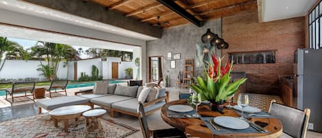 A modern interior with a dining area, poolside seating, and a brick wall.