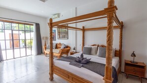 Um quarto espaçoso com uma cama de dossel, uma mesinha de cabeceira de madeira e uma janela grande com cortinas.