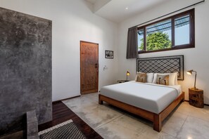 A bedroom with a large bed, a wooden door, a window with curtains, and a nightstand with a lamp. - Villa Maje by Alfred in Bali (Seminyak)