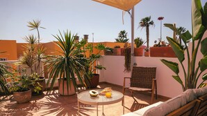A sunlit patio with a round table, a cushioned bench, and various potted plants. - Vacation apartment Matimar, Costa Calma, terrace, WiFi (Costa Calma)