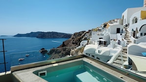 Piscina no terraço com vista para o mar e edifícios brancos.