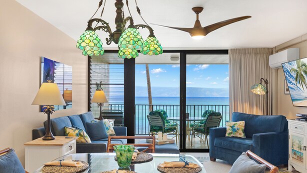 A living room with a glass table, blue sofas, and a view of the ocean. - 1bd Oceanfront gem with charm, views & Island vibe (Lahaina)