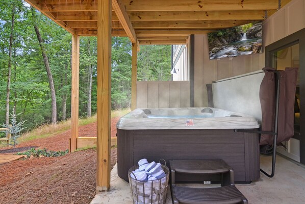 Un jacuzzi en un espacio exterior cubierto con una terraza de madera, rodeado de un bosque.