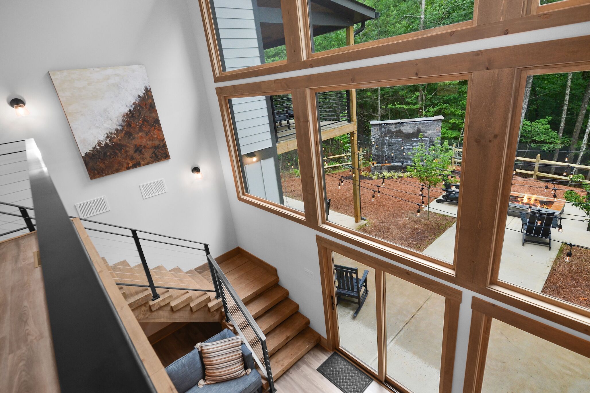 Un intérieur moderne avec un escalier, de grandes fenêtres et une vue sur une terrasse extérieure.