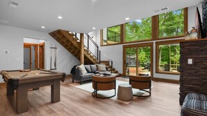 Un ampli saló amb billar, seients còmodes, una escala i grans finestres que ofereixen vistes a l'exterior.