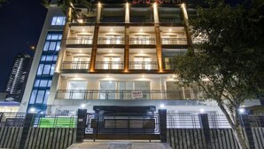 A multi-story hotel with a prominent entrance, a sign indicating a toilet facility, and a well-lit facade. - Hotel Noida Dreamz 144 (Noida)