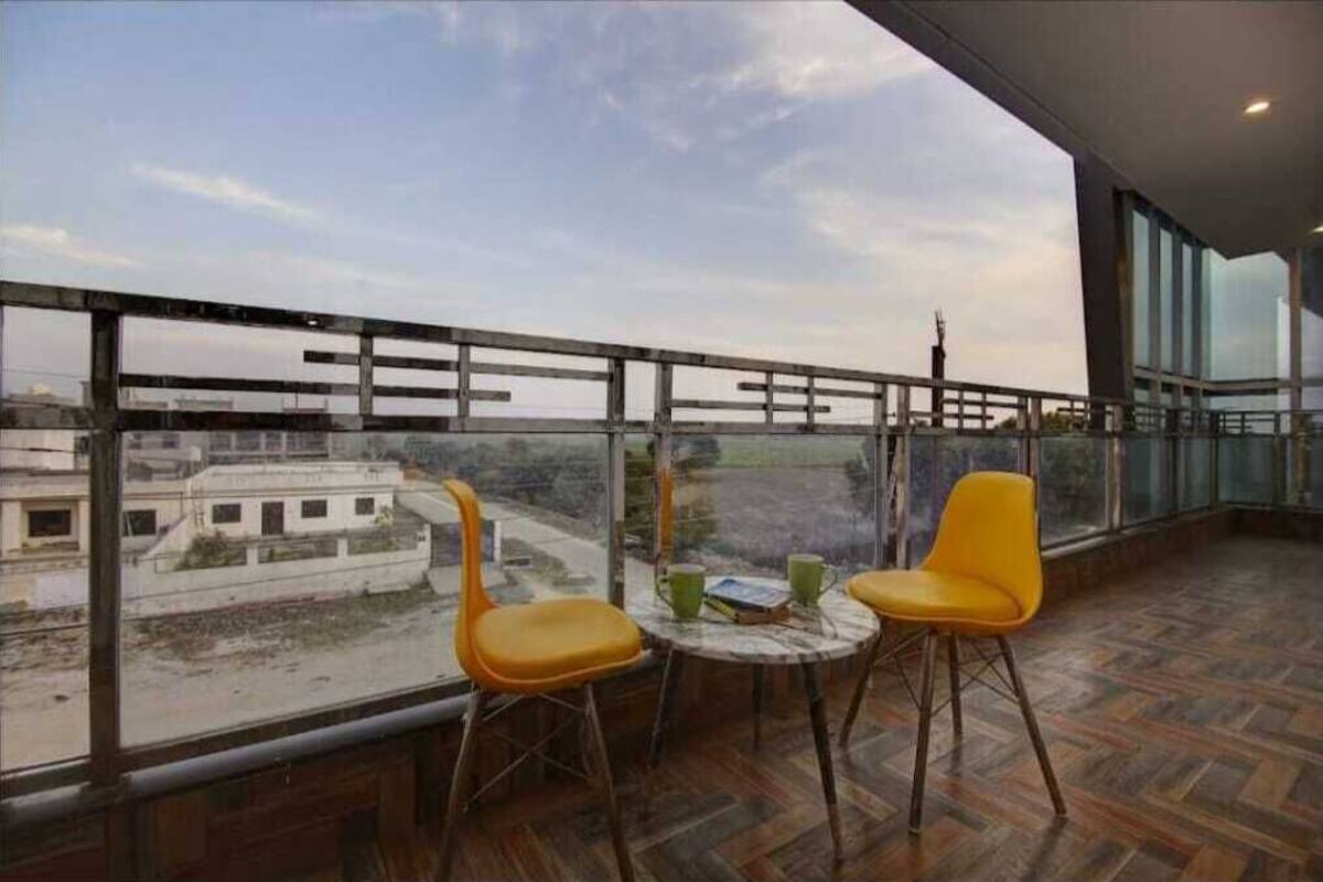 A balcony with two yellow chairs and a small table, overlooking a cityscape.